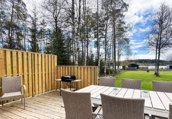 Buitenpatio met eettafel, stoelen en barbecue, uitkijkend op het grasveld en meer bij Hestra, Zweden.