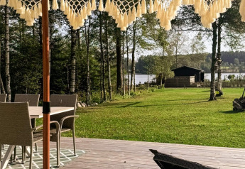 Terrasse mit Korbstühlen, Blick auf Wiese, Bäume und See beim 4-Sterne-Ferienhaus in Hestra, Schweden.