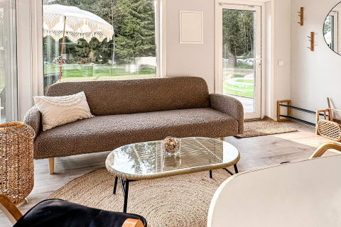 Lichte, moderne leefruimte met bruine sofa, glazen tafel en grote ramen in een 4-sterren vakantiewoning in Hestra, Zweden.