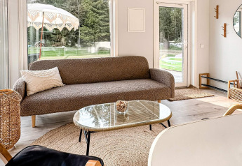 Lyst og moderne opholdsområde med brun sofa, sofabord og store vinduer på et 4-stjernet feriehus i Hestra, Sverige.