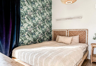 Slaapkamer in lodge met gevlochten hoofdeinde, tropisch behang en warme sfeer in Hestra, Zweden.
