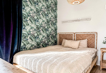 Dormitorio en una cabaña con cabecero de mimbre, papel tropical y luz suave en Hestra, Suecia.