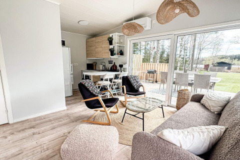 Moderne opholdsstue med åbent køkken og store vinduer i en lodge i Hestra, Sverige, med udsigt til have.