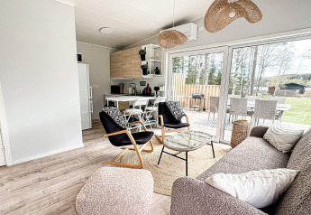 Moderne opholdsstue med åbent køkken og store vinduer i en lodge i Hestra, Sverige, med udsigt til have.