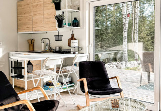 Moderne, kompakt køkken og stue med store vinduer ud til træterrasse og natur i et svensk feriehus.