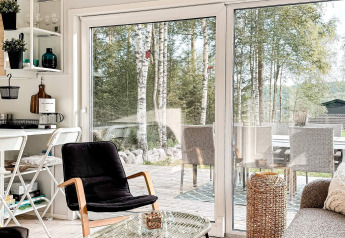Heldere, moderne leefruimte in een vakantiehuis in Hestra, Zweden, met grote schuiframen naar het terras.