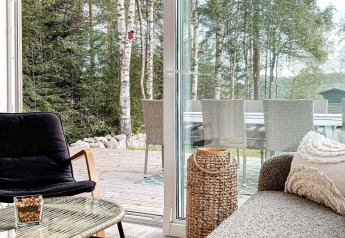 Lichte, gezellige woonkamer met modern meubilair en uitzicht op terras en bos bij lodge in Hestra, Zweden.