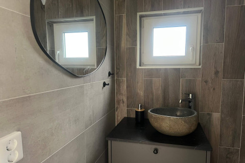 Bagno moderno con lavabo in pietra, specchio rotondo e finestra piccola in una casa vacanze a Hestra, Svezia.