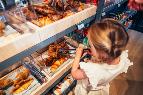 Bambino prende croissant con le pinze nel reparto panetteria di Eurocamping Vessem BV, Brabante Settentrionale, Paesi Bassi.