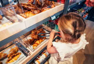 Bambino prende croissant con le pinze nel reparto panetteria di Eurocamping Vessem BV, Brabante Settentrionale, Paesi Bassi.