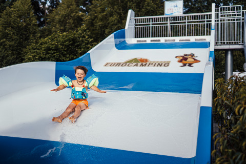 Een kind met zwembandjes glijdt van een waterglijbaan bij Eurocamping Vessem in Noord-Brabant, Nederland.