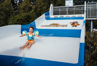 Un bambino con braccioli scivola su uno scivolo d'acqua a Eurocamping Vessem nei Paesi Bassi.