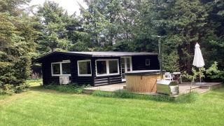 Casa vacanza nera per sei persone a Idestrup, circondata da alberi con terrazza, vasca e ombrellone.