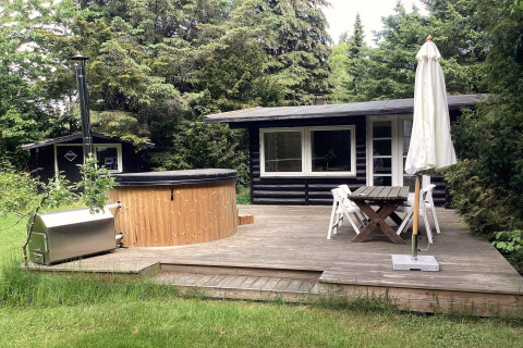 Terrazza in legno con vasca idromassaggio, tavolo da giardino e ombrellone a Idestrup, Danimarca.