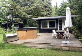 Terrazza in legno con vasca idromassaggio, tavolo da giardino e ombrellone a Idestrup, Danimarca.