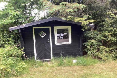 Een zwart tuinhuis omringd door groen bij het 6-persoons vakantiehuis in Idestrup, Denemarken.