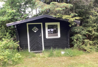 A black garden shed surrounded by greenery at the 6 person holiday home in Idestrup, Denmark.