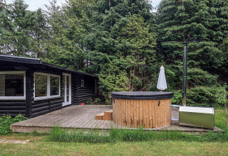 Terraza exterior de madera con jacuzzi frente a cabaña en casa de vacaciones para 6 personas en Idestrup, Dinamarca.