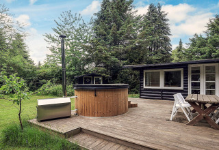 Træterrasse med spabad og havemøbler ved feriehus i Idestrup, Danmark, omgivet af frodig skov.