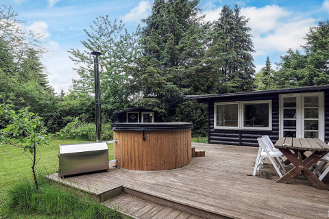 Houten terras met bubbelbad en tuinset bij vakantiehuis in Idestrup, Denemarken, tussen groen.