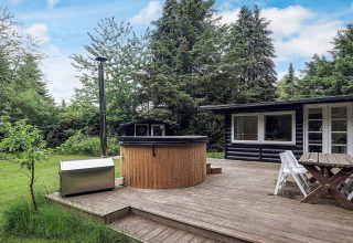 Houten terras met bubbelbad en tuinset bij vakantiehuis in Idestrup, Denemarken, tussen groen.