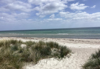 Strandudsigt med klitter, sand og græs under en delvist skyet himmel ved Idestrup, Danmark.