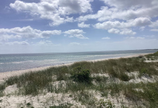 Spiaggia tranquilla con dune erbose e mare a Idestrup, Danimarca, sotto un cielo parzialmente nuvoloso.