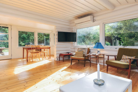 Salon lumineux d'une location de vacances à Idestrup, Danemark, avec fenêtres panoramiques et mobilier bois.