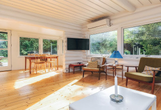 Salon lumineux d'une location de vacances à Idestrup, Danemark, avec fenêtres panoramiques et mobilier bois.