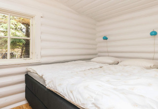 Dormitorio acogedor con cama doble, paredes de madera blanca y ventana en una casa rural en Idestrup, Dinamarca.