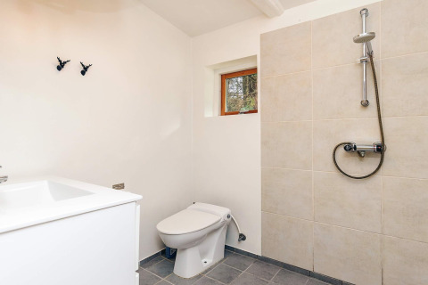 Moderne badeværelse i feriebolig i Idestrup, Danmark, med bruseniche, toilet og håndvask.
