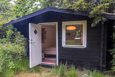 Piccola baita nera con porta bianca aperta, immersa nel verde al lodge per 6 persone a Idestrup, Danimarca.