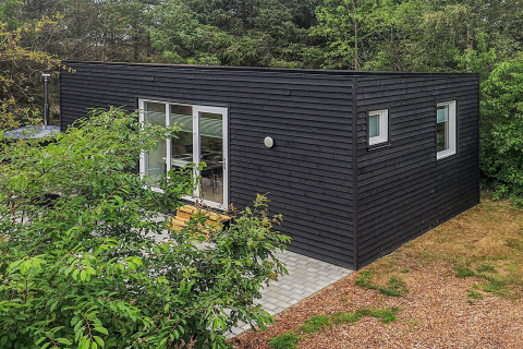 Cabaña negra moderna de vacaciones para 5 personas en Pandrup, Dinamarca, rodeada de árboles y terraza.