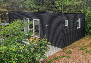 Cabaña negra moderna de vacaciones para 5 personas en Pandrup, Dinamarca, rodeada de árboles y terraza.