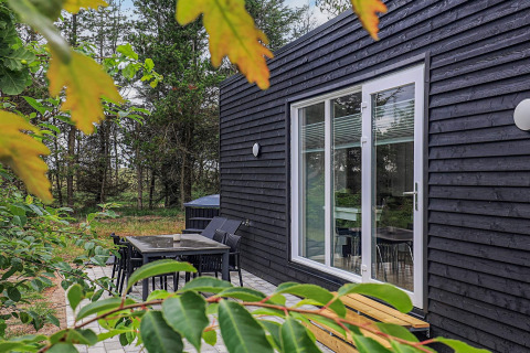 Cabaña negra en Pandrup, Dinamarca, con terraza exterior, muebles de jardín y vista al bosque verde.