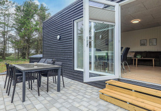 Zona de comedor exterior y terraza en una cabaña moderna de vacaciones en Pandrup, Dinamarca, con bosque.