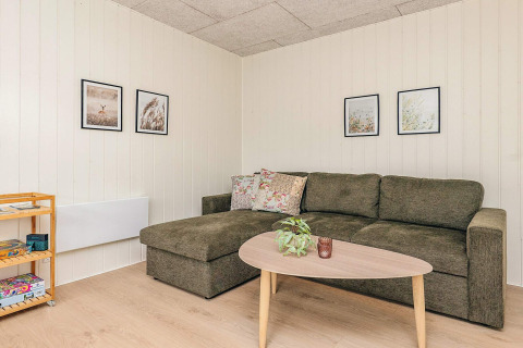 Sala de estar con sofá verde, mesa de centro, planta, cuadros y estante en una cabaña en Pandrup, Dinamarca.