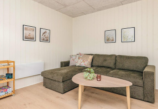 Sala de estar con sofá verde, mesa de centro, planta, cuadros y estante en una cabaña en Pandrup, Dinamarca.