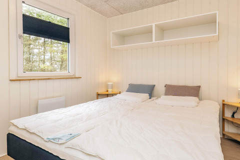 Dormitorio con cama doble, mesitas de noche, lámparas y estanterías en cabaña en Pandrup, Dinamarca.