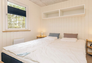 Dormitorio con cama doble, mesitas de noche, lámparas y estanterías en cabaña en Pandrup, Dinamarca.