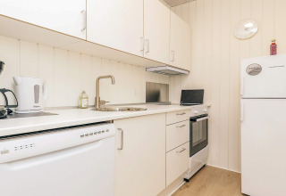 Cocina moderna blanca en una casa de vacaciones con lavavajillas, hervidor, cocina y refrigerador en Pandrup.