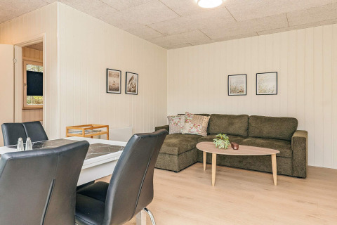 Salón luminoso en una cabaña vacacional en Pandrup, Dinamarca, con sofá rinconero y comedor moderno.