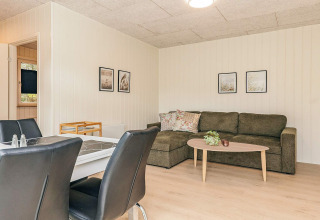 Salón luminoso en una cabaña vacacional en Pandrup, Dinamarca, con sofá rinconero y comedor moderno.