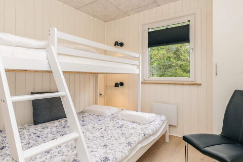 Dormitorio luminoso con litera, cama individual, silla y ventana en una cabaña en Pandrup, Dinamarca.