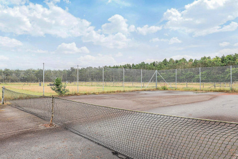 Pista de tenis abandonada con red caída y vegetación alrededor en un parque vacacional en Pandrup, Dinamarca.