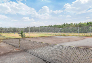 Pista de tenis abandonada con red caída y vegetación alrededor en un parque vacacional en Pandrup, Dinamarca.