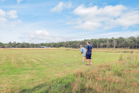 Dos personas juegan croquet en un amplio campo de césped junto a una cabaña en Pandrup, Dinamarca.