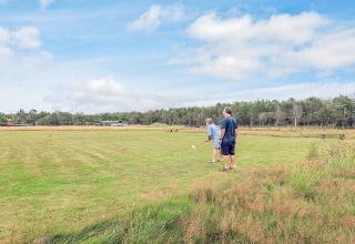 Dos personas juegan croquet en un amplio campo de césped junto a una cabaña en Pandrup, Dinamarca.