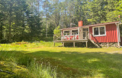 Cabaña roja Peaceful Cabin cerca de Furufjall Trail, Suecia, rodeada de bosque y césped verde.