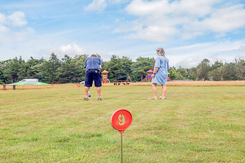 Dos personas juegan croquet en un campo verde de una casa de vacaciones en Pandrup, Dinamarca, con parque al fondo.